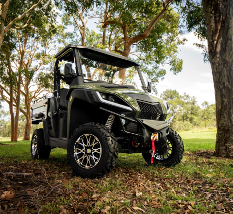 Black off-road utility vehicle with large tires parked in a sunlit forest clearing.